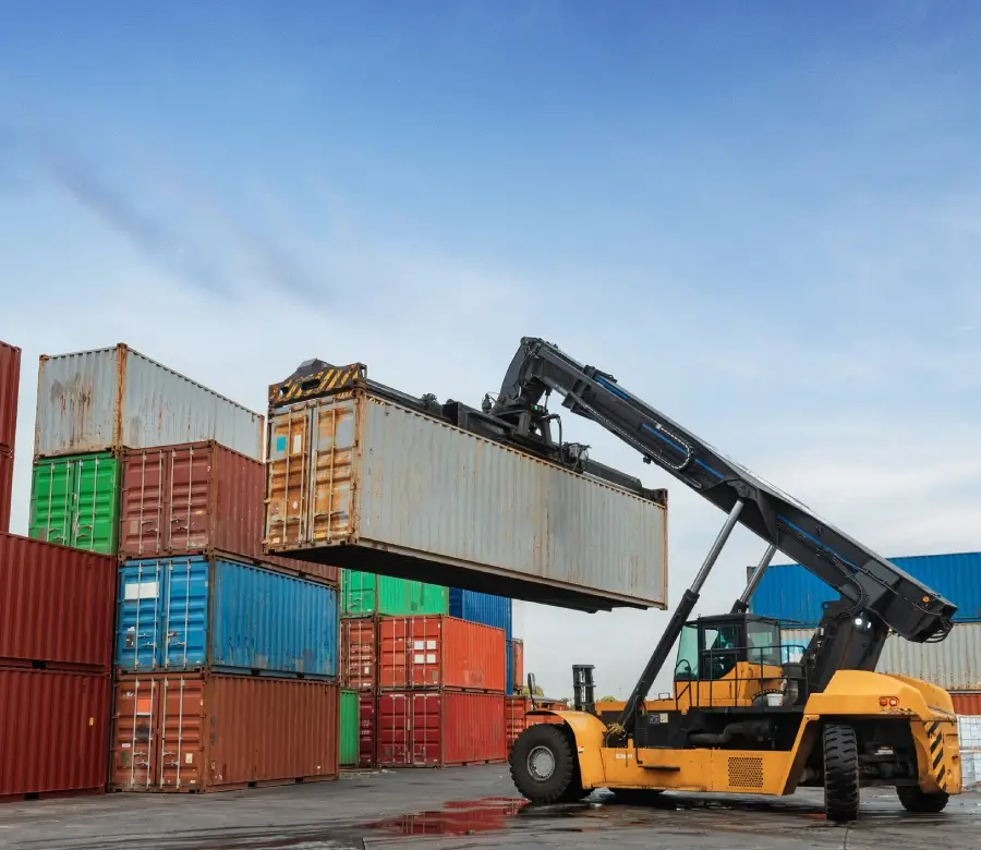A forklift is lifting a shipping container at a busy port.