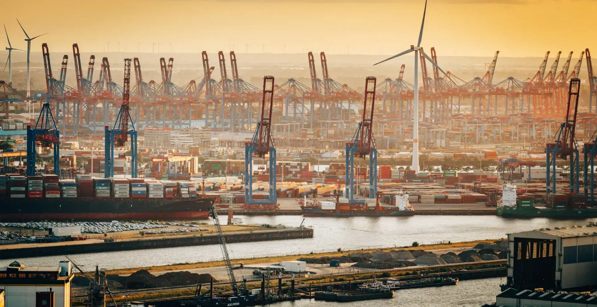 Sunset container port with cranes and wind turbine